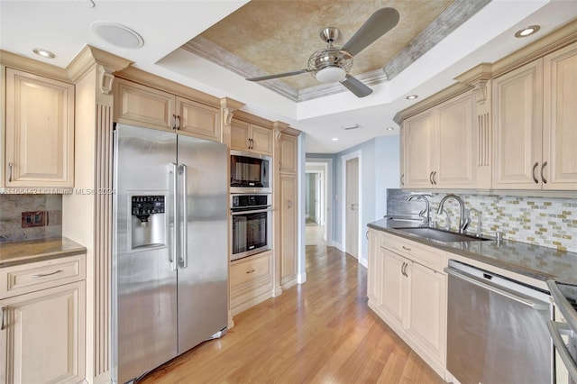 kitchen with appliances with stainless steel finishes, light wood-type flooring, backsplash, a raised ceiling, and sink