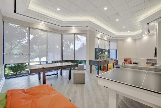 recreation room featuring a tray ceiling, crown molding, and light wood-type flooring