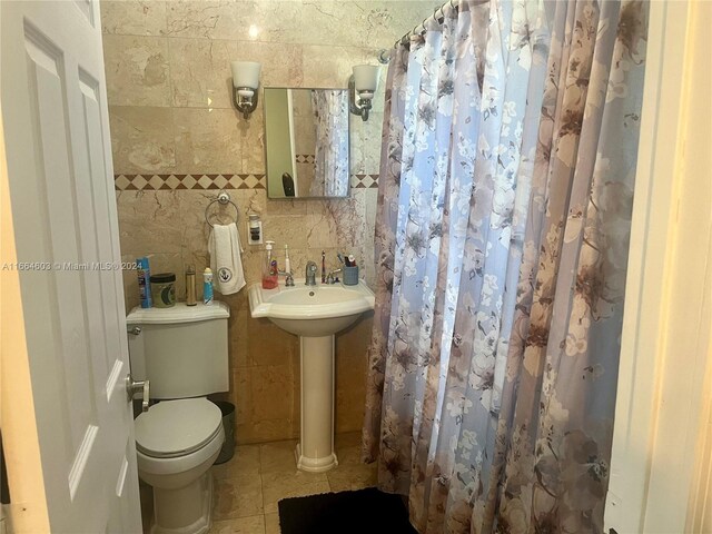 bathroom with tile walls, curtained shower, tile patterned floors, and toilet