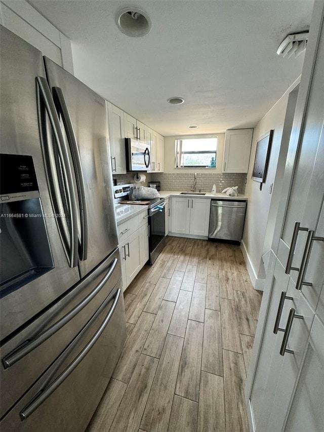 kitchen featuring sink, tasteful backsplash, light hardwood / wood-style flooring, white cabinetry, and appliances with stainless steel finishes