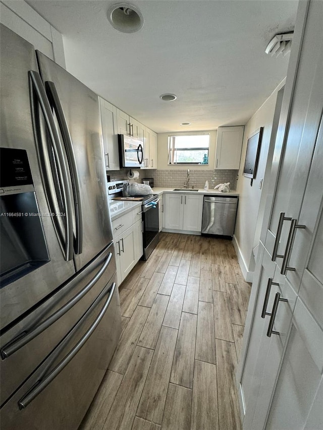 kitchen featuring white cabinets, sink, appliances with stainless steel finishes, light wood-type flooring, and decorative backsplash