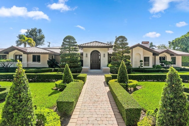 mediterranean / spanish home with a tiled roof, a front lawn, and stucco siding