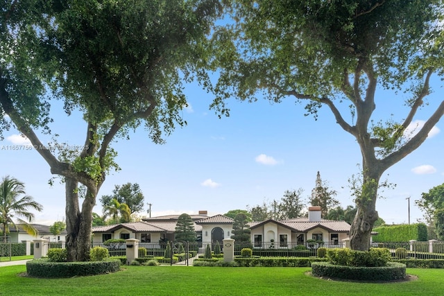 view of front facade featuring a tiled roof, a fenced front yard, a chimney, and a front yard