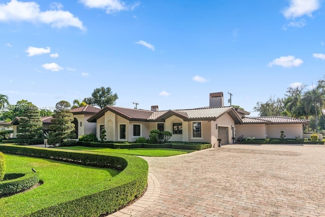 mediterranean / spanish-style house featuring stucco siding, a chimney, decorative driveway, and a tiled roof