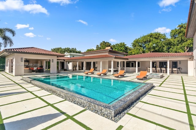 back of house featuring an outdoor fire pit, an outdoor pool, a patio, a tile roof, and stucco siding