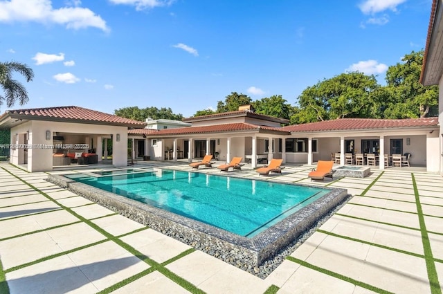 rear view of property with a patio area, an outdoor fire pit, an outdoor pool, and a tiled roof