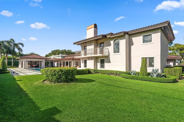 rear view of property featuring a chimney, a yard, a balcony, and stucco siding