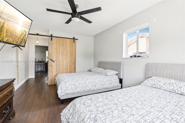 bedroom featuring ceiling fan, a textured ceiling, dark wood-type flooring, and a barn door