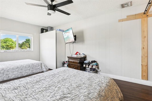 bedroom with a textured ceiling, wooden walls, hardwood / wood-style floors, and ceiling fan