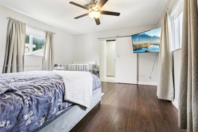 bedroom featuring a barn door, dark wood-type flooring, and ceiling fan