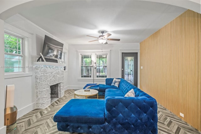 living room featuring ceiling fan, a stone fireplace, wood walls, and light parquet flooring