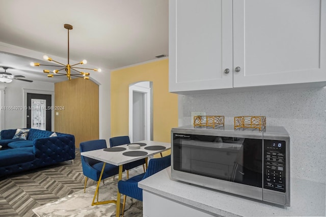 kitchen with white cabinets, ceiling fan with notable chandelier, and decorative backsplash