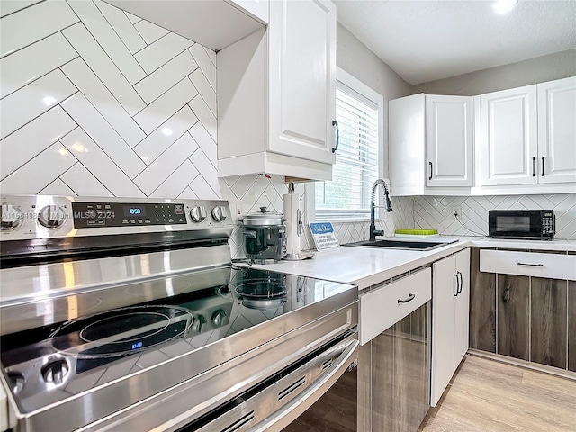 kitchen with stainless steel range with electric cooktop, light wood-type flooring, white cabinetry, and sink