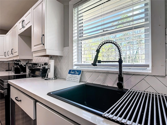 kitchen with stainless steel range with electric cooktop, white cabinets, backsplash, and sink