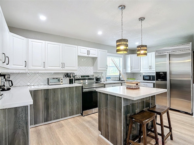 kitchen with appliances with stainless steel finishes, light hardwood / wood-style floors, white cabinetry, a breakfast bar, and a center island