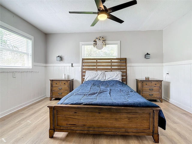 bedroom with multiple windows, a textured ceiling, ceiling fan, and light hardwood / wood-style flooring