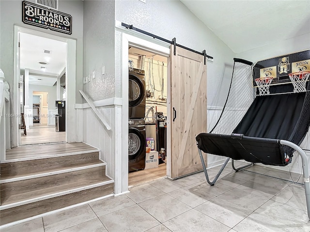 miscellaneous room with stacked washer / drying machine, a barn door, and light tile patterned floors