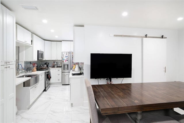 kitchen featuring sink, tasteful backsplash, white cabinetry, stainless steel appliances, and a barn door