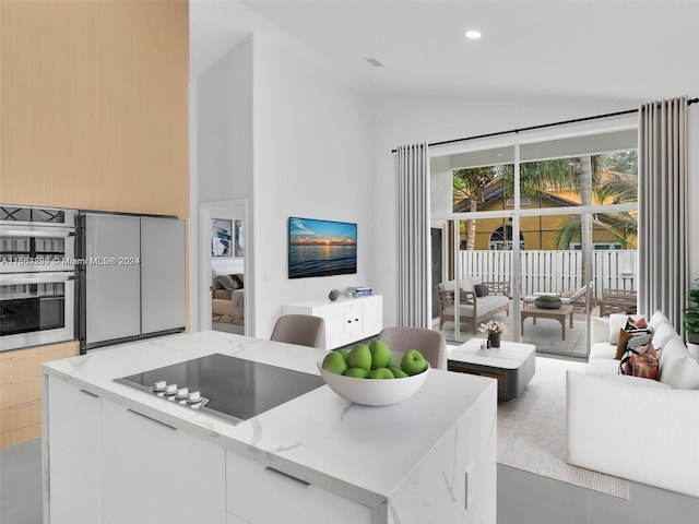 kitchen featuring a center island, white cabinetry, lofted ceiling, stainless steel appliances, and light stone countertops