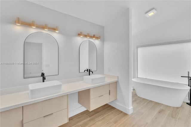 bathroom featuring wood-type flooring, vanity, a washtub, and vaulted ceiling