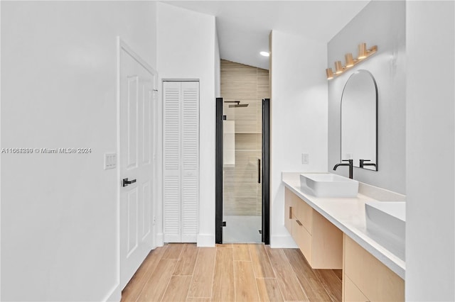 bathroom with wood-type flooring, vaulted ceiling, a shower with shower door, and vanity