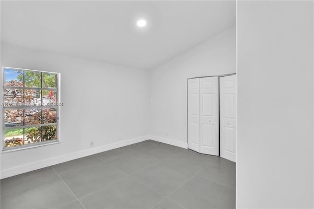 unfurnished bedroom with vaulted ceiling, dark tile patterned floors, and a closet