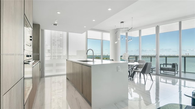 kitchen with expansive windows, a kitchen island with sink, sink, and a water view