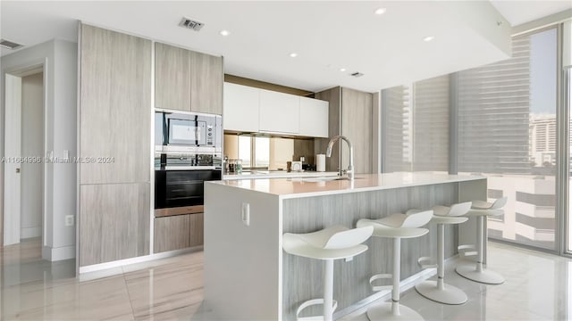 kitchen featuring appliances with stainless steel finishes, white cabinets, a breakfast bar area, a wealth of natural light, and a kitchen island with sink