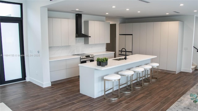 kitchen with white cabinetry, a kitchen island with sink, wall chimney exhaust hood, and sink