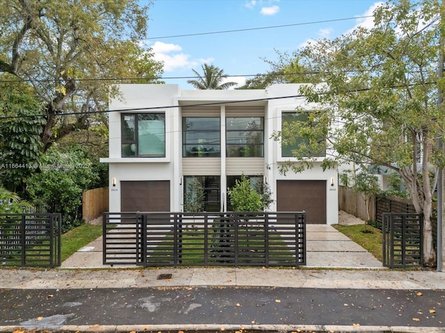 contemporary home featuring a fenced front yard, a gate, a garage, and stucco siding