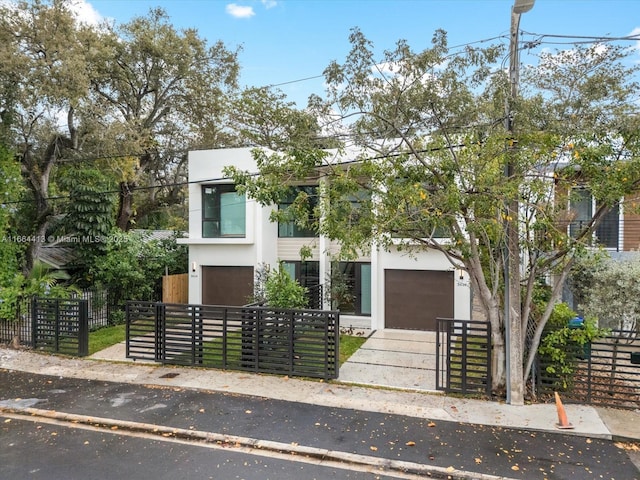 contemporary home featuring a garage, driveway, a fenced front yard, and stucco siding