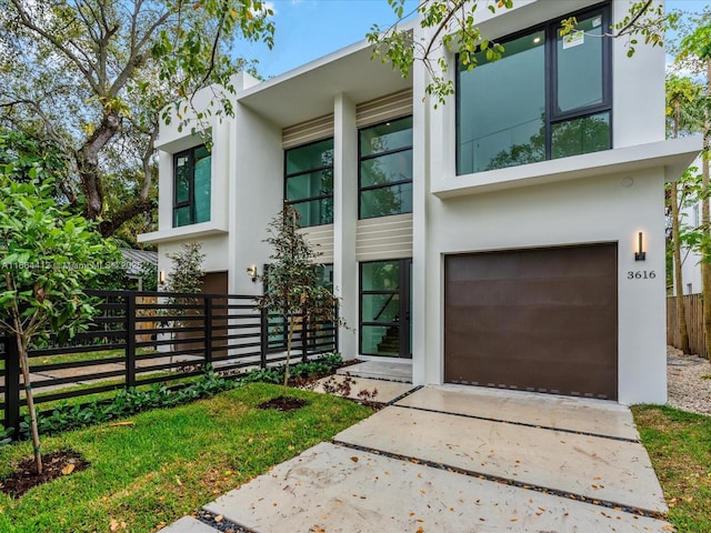 modern home with a garage, concrete driveway, fence, and stucco siding