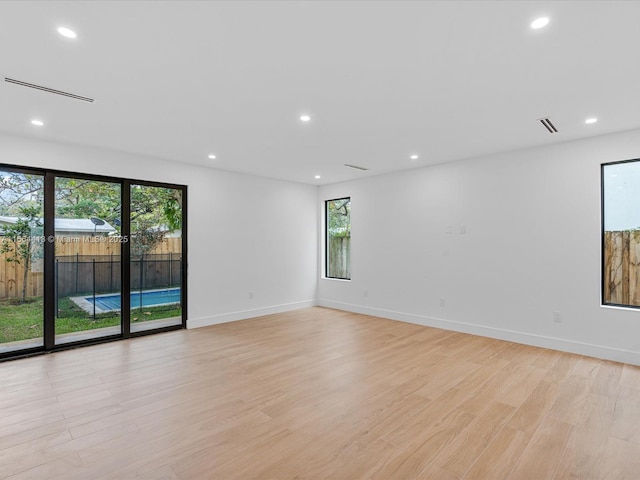 empty room with light wood finished floors, a wealth of natural light, and recessed lighting