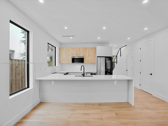 kitchen featuring light wood finished floors, stainless steel appliances, light countertops, a sink, and a peninsula