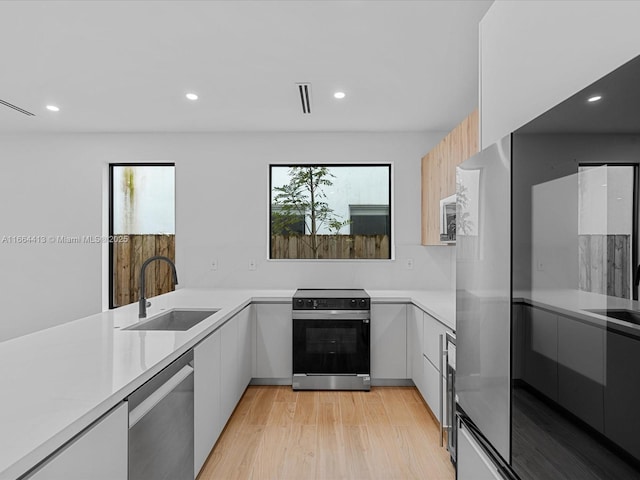 kitchen featuring dishwasher, electric stove, modern cabinets, light countertops, and a sink