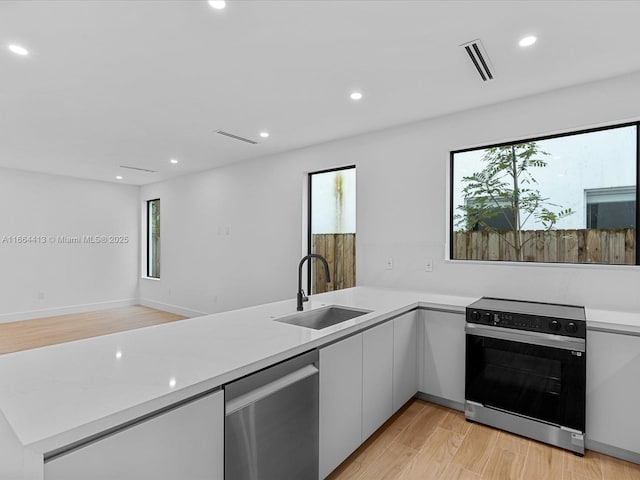 kitchen featuring dishwasher, light countertops, a sink, and range with electric stovetop