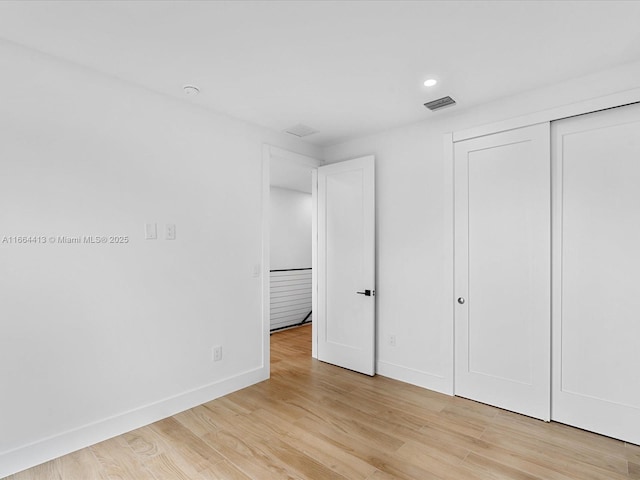 unfurnished bedroom with light wood finished floors, baseboards, visible vents, and a closet