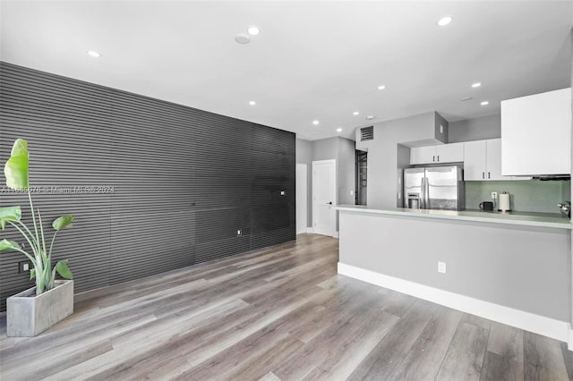 kitchen with kitchen peninsula, stainless steel refrigerator with ice dispenser, light hardwood / wood-style flooring, and white cabinetry