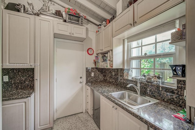 kitchen featuring tasteful backsplash, white cabinets, beam ceiling, dark stone counters, and sink