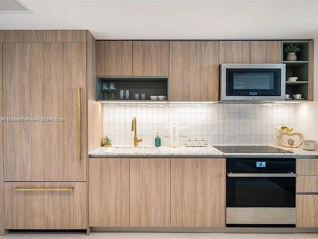 kitchen featuring light stone counters, light brown cabinets, appliances with stainless steel finishes, and backsplash