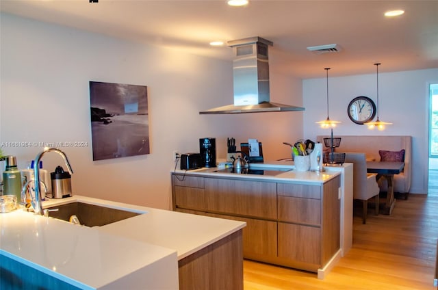 kitchen featuring light hardwood / wood-style floors, sink, island range hood, black cooktop, and decorative light fixtures