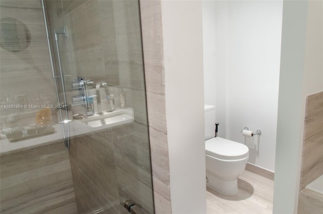 bathroom featuring hardwood / wood-style floors, a shower with shower door, and toilet