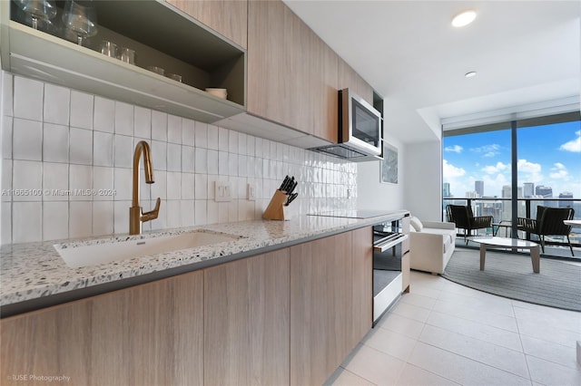kitchen with appliances with stainless steel finishes, a sink, decorative backsplash, light tile patterned floors, and modern cabinets