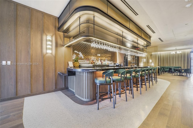 bar featuring visible vents, wood finished floors, wooden walls, a community bar, and a notable chandelier