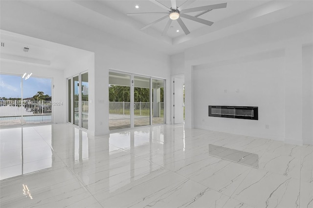 empty room with heating unit, a healthy amount of sunlight, a tray ceiling, and ceiling fan