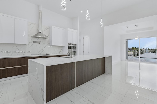 kitchen featuring decorative backsplash, an island with sink, white cabinets, island range hood, and decorative light fixtures