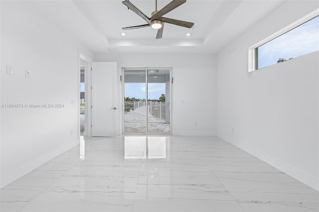 empty room featuring a healthy amount of sunlight, a tray ceiling, and ceiling fan