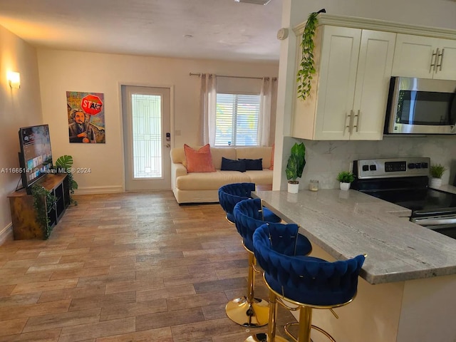 kitchen with light stone counters, appliances with stainless steel finishes, light wood-type flooring, and tasteful backsplash