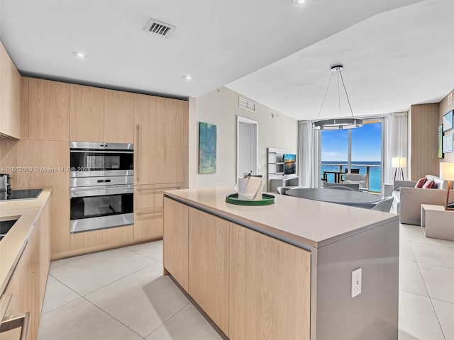 kitchen featuring light brown cabinets, light tile patterned flooring, hanging light fixtures, a center island, and stainless steel double oven