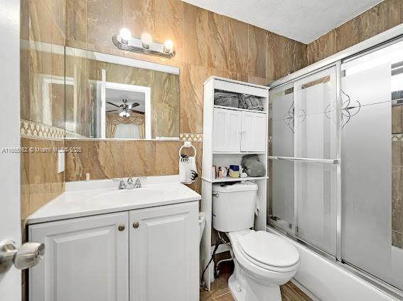 bathroom featuring toilet, shower / bath combination with glass door, tile walls, and vanity